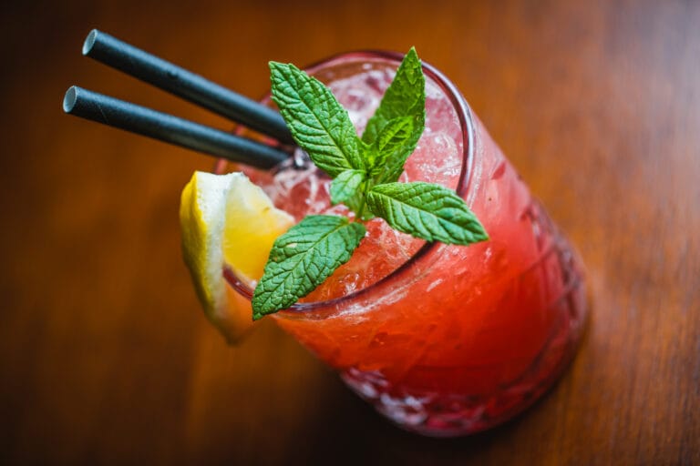 Close-up of a pink cocktail with fresh mint, lemon wedge and ice.